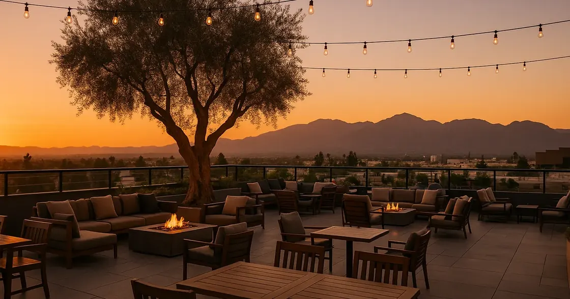 Open-air rooftop restaurant terrace at sunset built around an olive tree with fire pits and San Gabriel Mountain views
